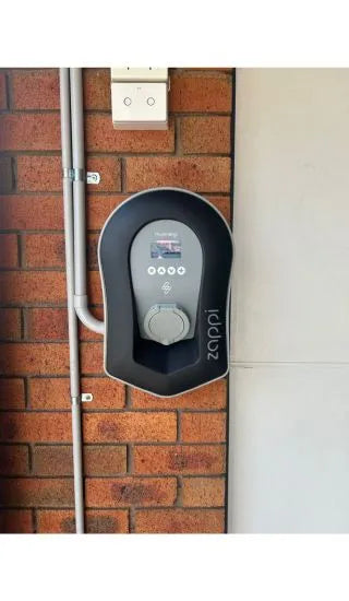 Black Zappi EV charger installed on a brick wall