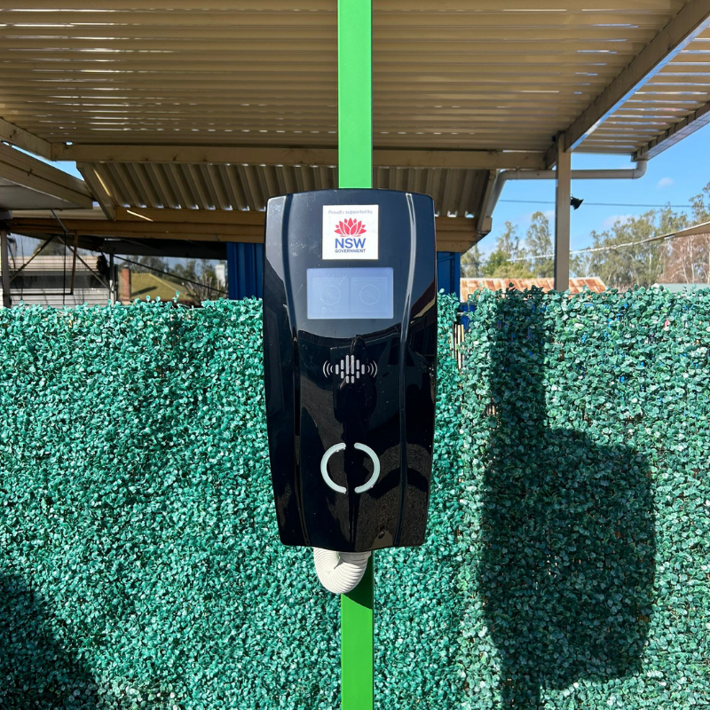 Black EV charging device with NSW logo on a green post