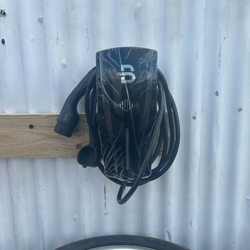 Black Beny EV charger on a wooden board against a corrugated metal