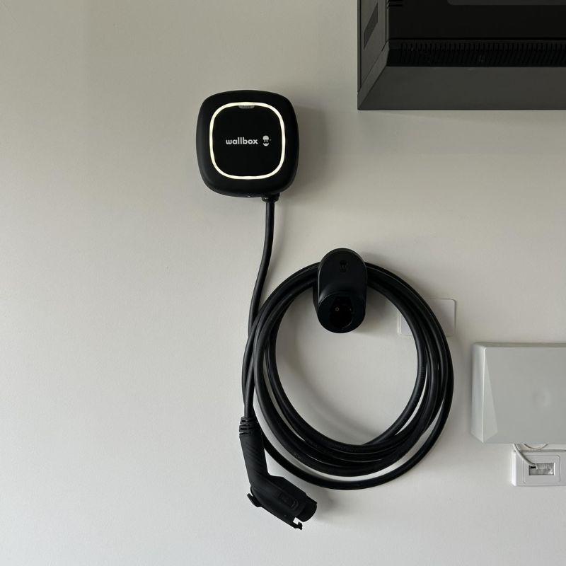 Black wallbox electric vehicle charging on a white wall.