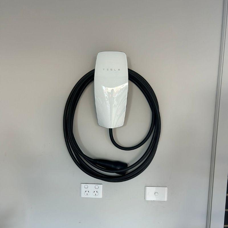 Tesla electric vehicle charging cable attached on a white wall.