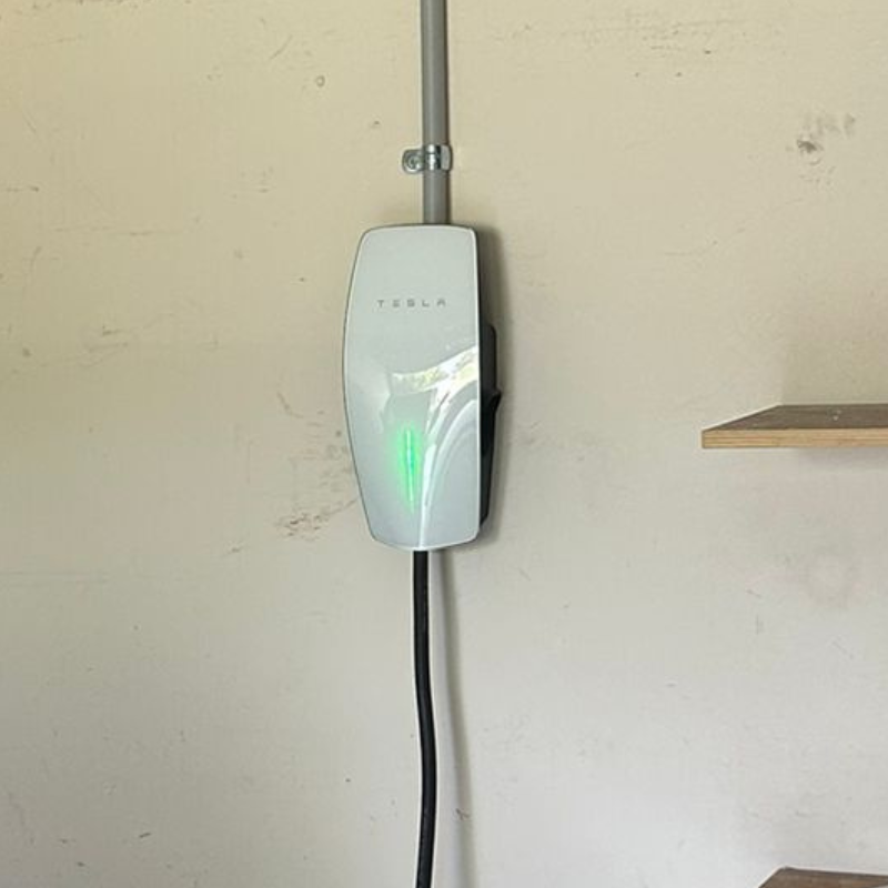 white tesla wall connector with green led light, attached to a cream wall