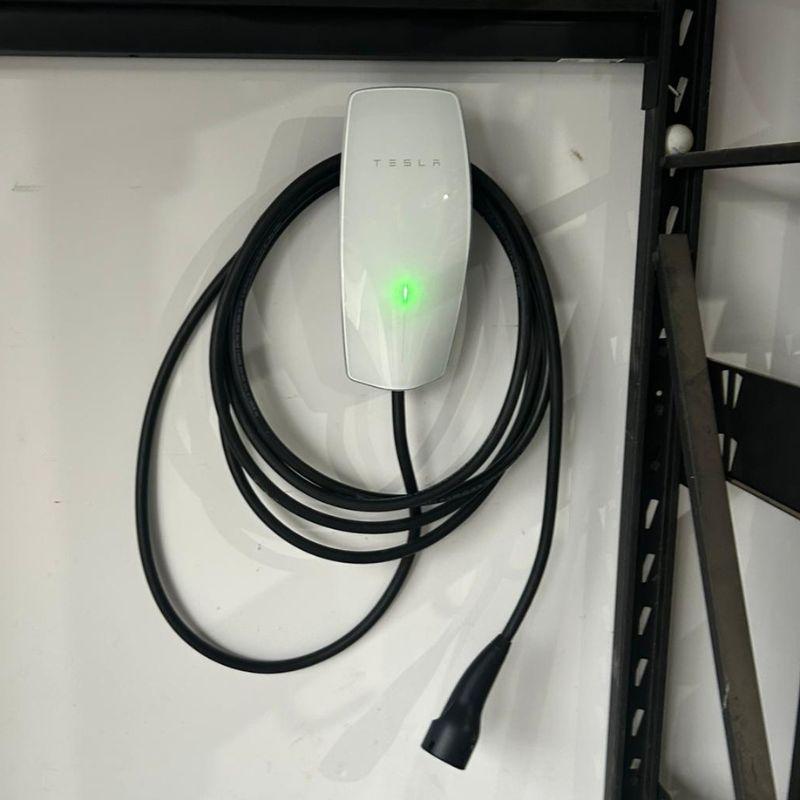 Tesla electric vehicle charging cable and wall adapter on a white surface.