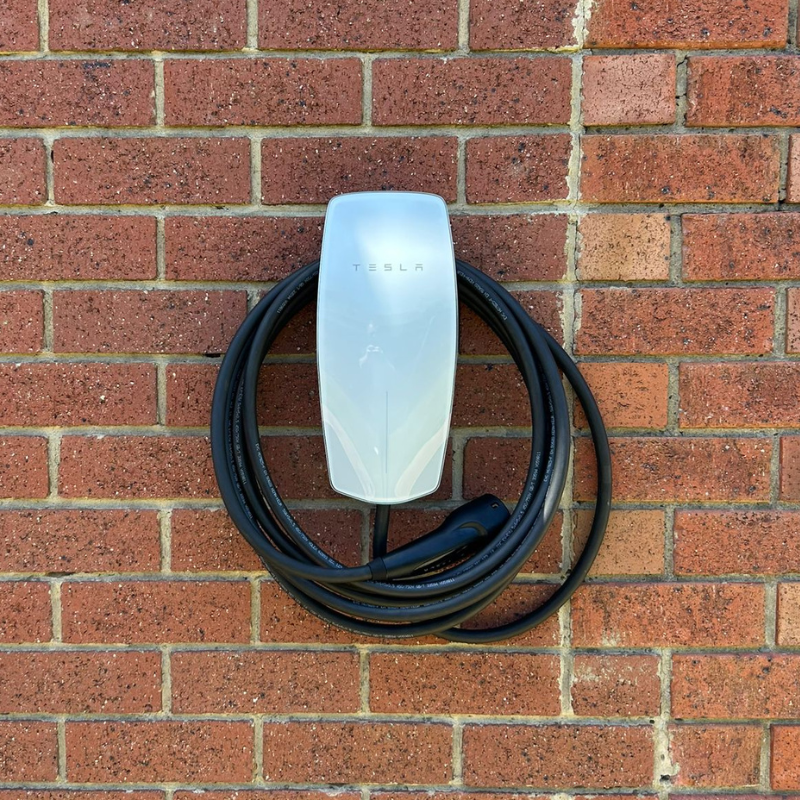 White Tesla Wall Connector EV charger mounted on a brick wall